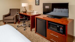 Habitación de hotel con cama, escritorio con computadora, silla, lámpara, televisor y microondas.