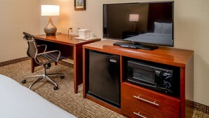 Habitación de hotel con un escritorio de madera, televisor, mini refrigerador, microondas, una silla y una cama.