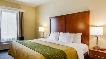 A hotel room with a large bed, two bedside lamps, a wooden headboard, and a window with curtains.