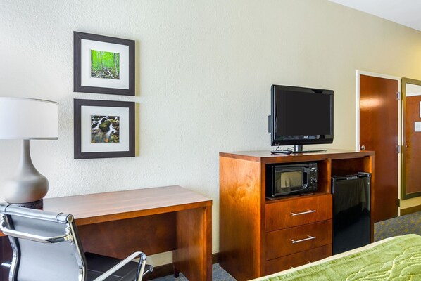 Habitación de hotel con escritorio de madera, una silla, televisor, microondas y refrigerador. Hay cuadros en la pared.