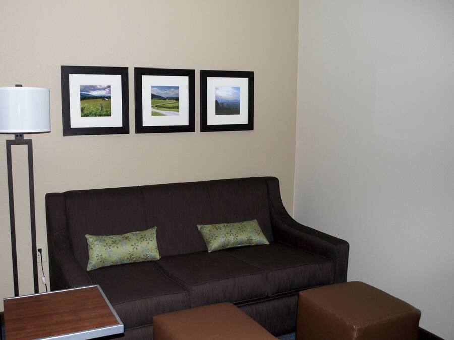 A dark brown sofa with floral cushions, a small wooden side table, and a brown ottoman. Three framed landscape pictures are hung on the wall above the sofa.