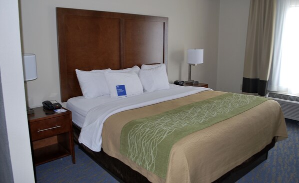 Habitación de hotel con una cama grande, cabecera de madera, mesita de noche con lámpara y teléfono.