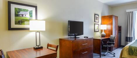 Habitación de hotel con un escritorio de madera, un televisor, una silla, una cama y un cuadro en la pared.
