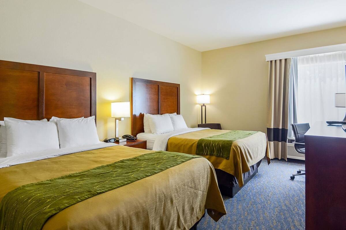 Habitación de hotel con dos camas, un escritorio, una silla y una lámpara.