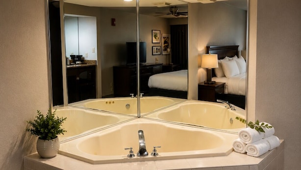 A corner bathroom with a large mirror, a bathtub, and a potted plant. - Country Inn & Suites by Radisson, Biloxi-Ocean Springs, MS (Ocean Springs)
