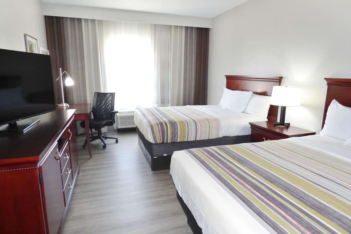 A hotel room with two beds, a desk with a television, a chair, and a window with curtains.