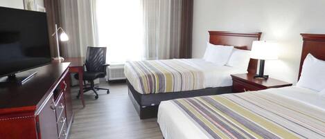A hotel room with two beds, a desk with a television, a chair, and a window with curtains.
