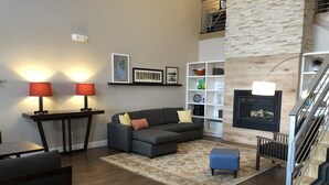 A modern living room with a gray sectional sofa, two red lamps, a white shelving unit, and a fireplace. - Country Inn & Suites by Radisson, Rapid City, SD (Rapid City)