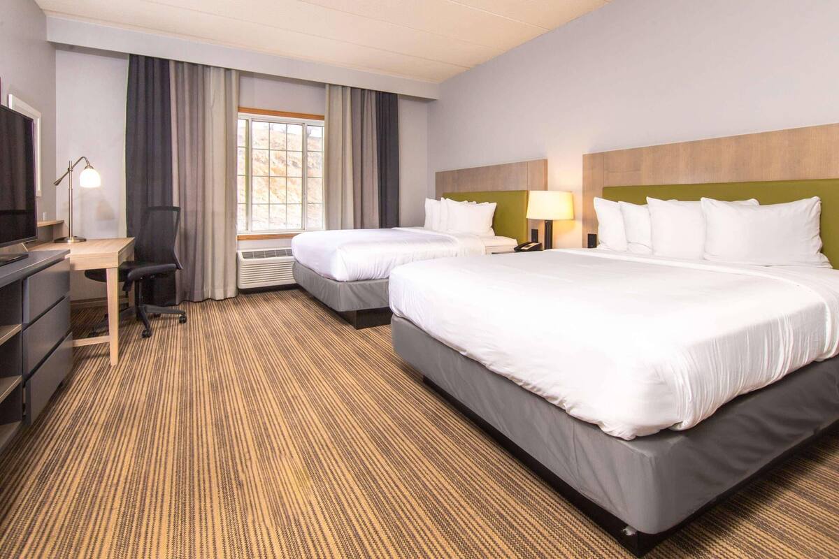 A hotel room with two beds, a desk, a chair, a TV, and a window with curtains.
