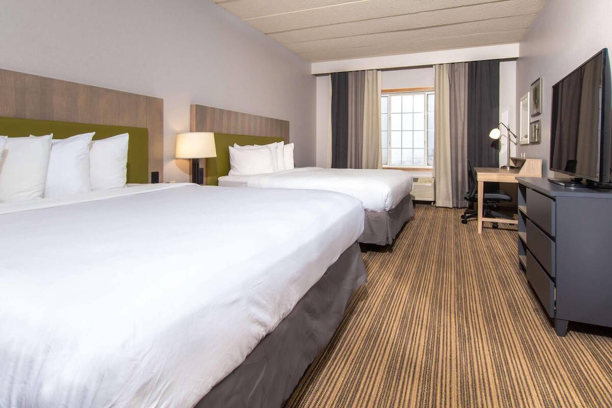 A hotel room with two beds, a desk, a TV, and a window with curtains.