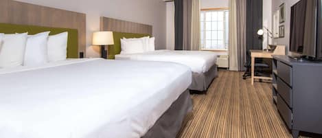 Habitación de hotel con dos camas, un escritorio, un televisor y una ventana con cortinas.