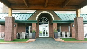 A brick building with a green roof, a covered entrance, and a white fence. - Country Inn & Suites by Radisson, Rapid City, SD (Rapid City)