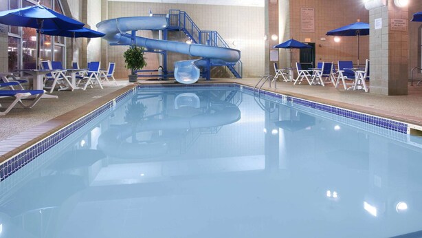 An indoor swimming pool with a water slide, lounge chairs, and umbrellas. - Country Inn & Suites by Radisson, Rapid City, SD (Rapid City)
