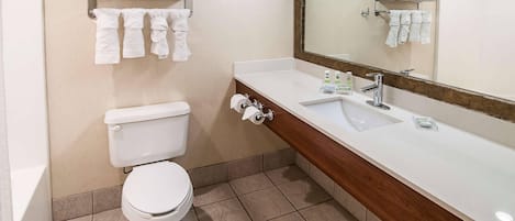 A bathroom with a toilet, a sink, a mirror, and towels on a shelf.