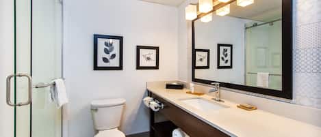 Een moderne badkamer met een douchecabine van glas, een wit toilet, een wastafel met spiegel en kunstwerken in lijsten aan de muur.