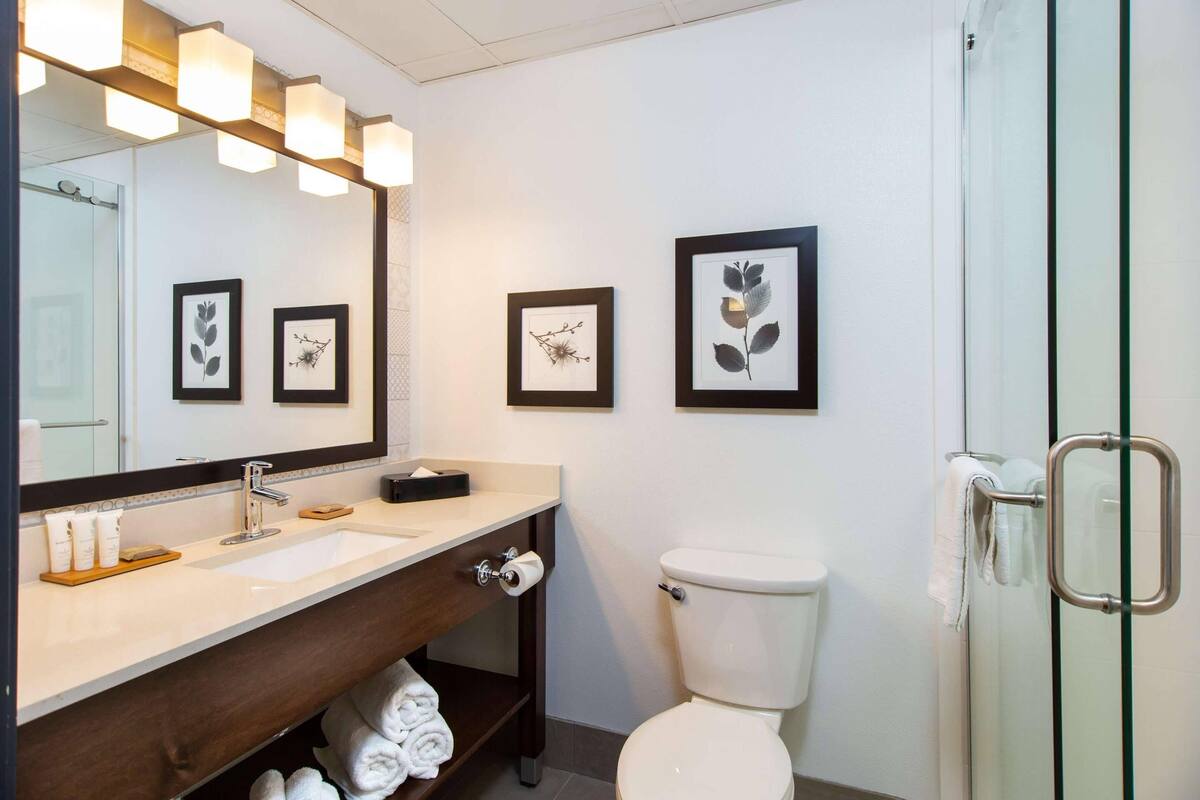 A modern bathroom with a large mirror, a sink, a toilet, and framed artwork on the wall.