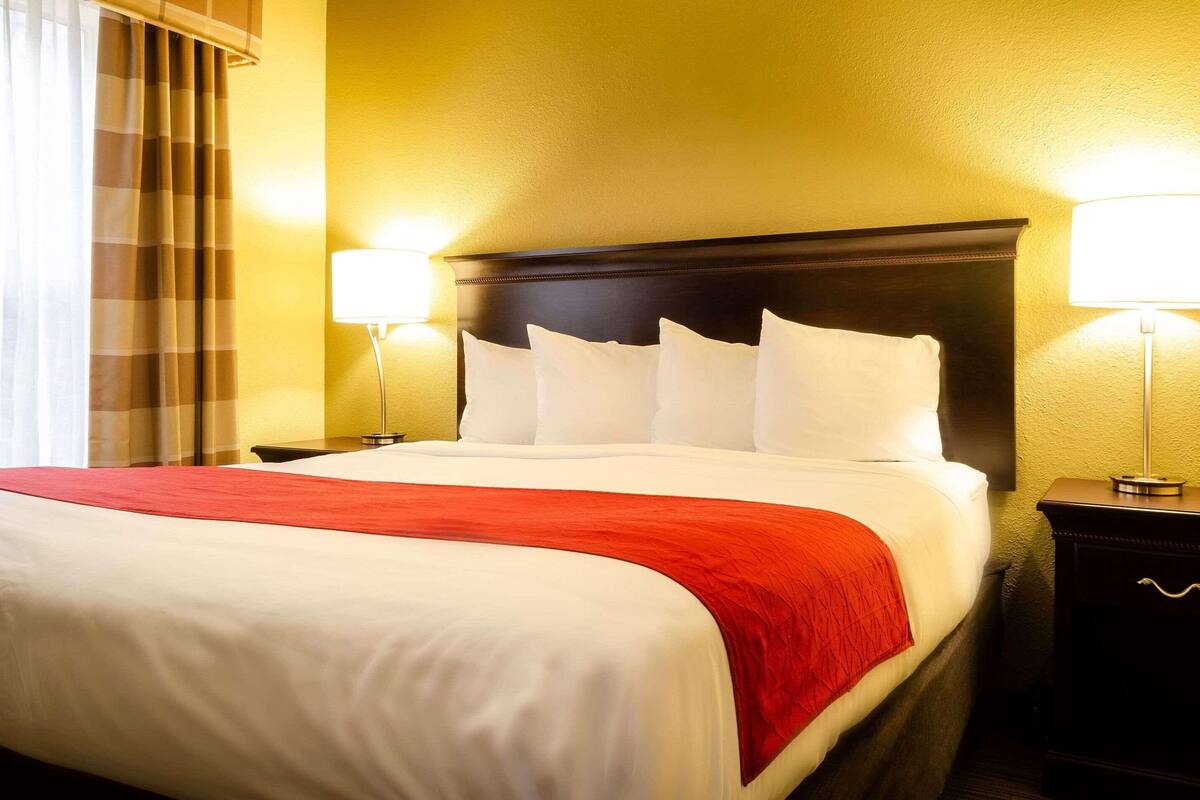 A neatly made bed with white and red bedding, two bedside lamps, and a dark headboard.