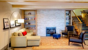 A cozy living room with a fireplace, a sofa, a coffee table, and a bookshelf. - Country Inn & Suites by Radisson, Tuscaloosa, AL (Tuscaloosa)