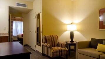 A hotel room with a striped armchair, a sofa, a lamp, and a bed with a curtain.