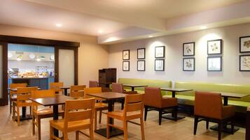 Un restaurante con mesas y sillas de madera, un banco verde y obras de arte enmarcadas en las paredes.