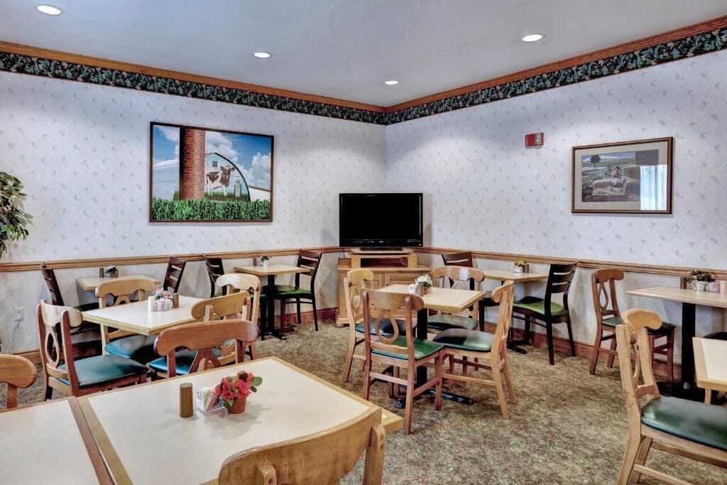 Un espace repas avec des tables et des chaises en bois, un téléviseur à écran plat et des tableaux encadrés aux murs.