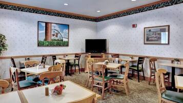 Un comedor con mesas y sillas de madera, un televisor de pantalla plana y cuadros en las paredes.