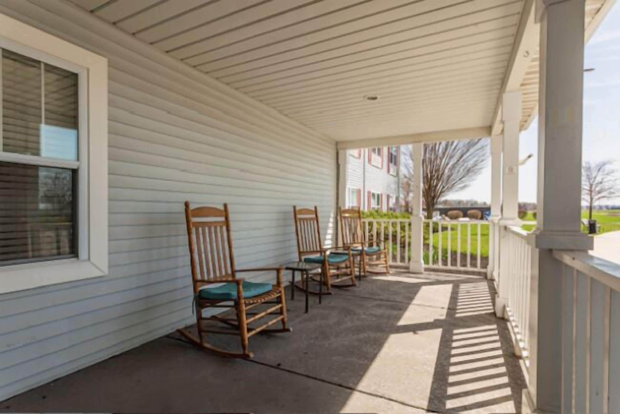 A covered porch with wooden rocking chairs and a white railing.