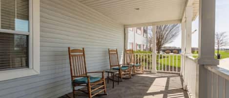 A covered porch with wooden rocking chairs and a white railing.