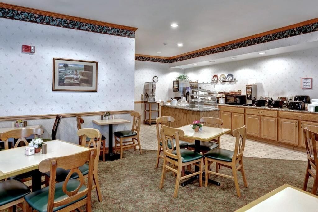 Un restaurante con sillas y mesas de madera, una zona de cocina y un cuadro enmarcado en la pared.