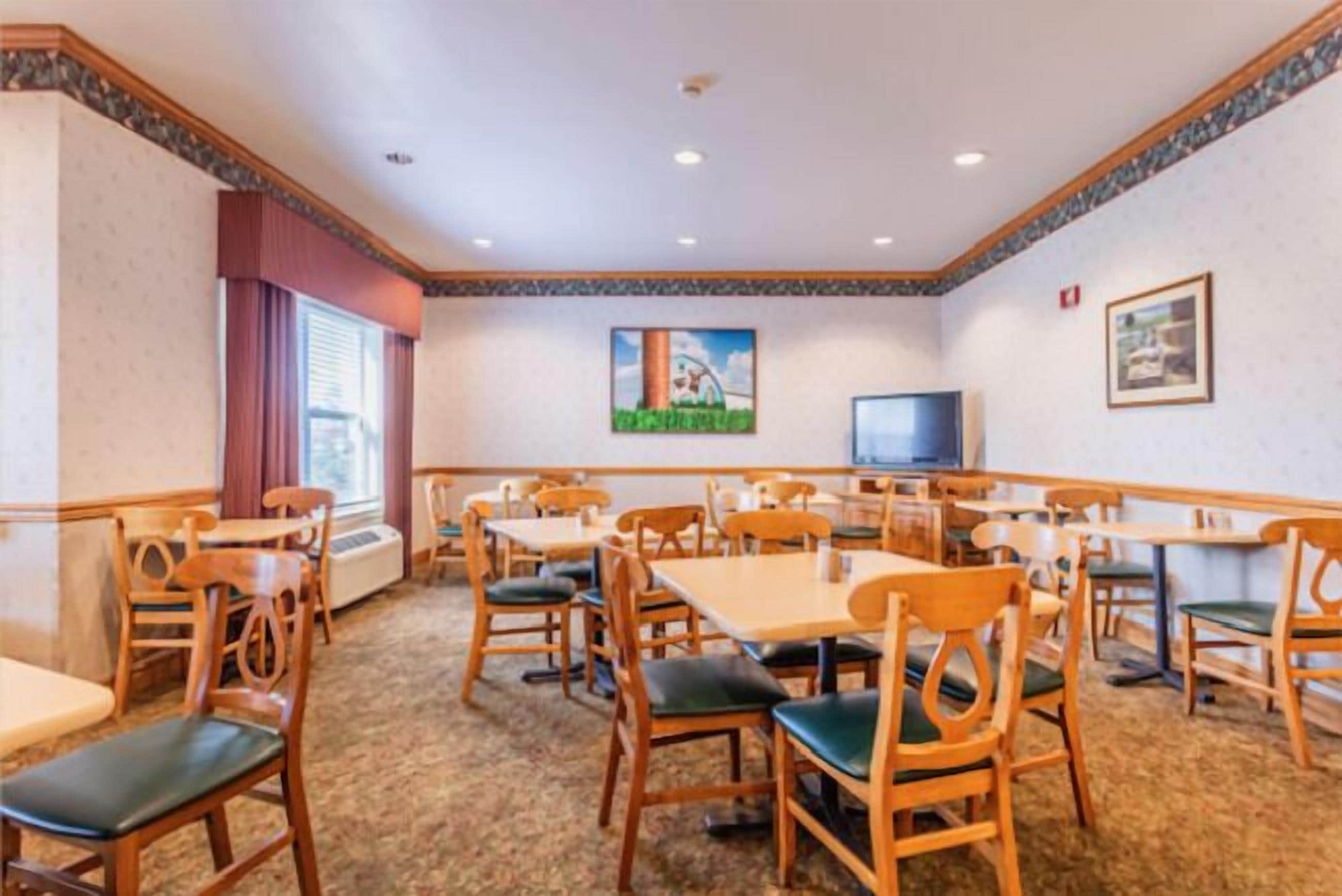 A hotel dining area with wooden tables and chairs, a television, and framed pictures on the walls.