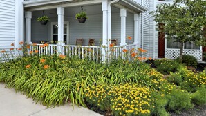 A white house with a porch, a white picket fence, and a garden with yellow and orange flowers.