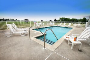 A pool area with white lounge chairs and a small table with drinks.