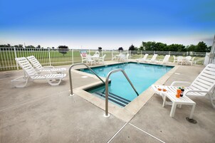 Zona de piscina con sillas de descanso blancas y una mesa con bebidas.