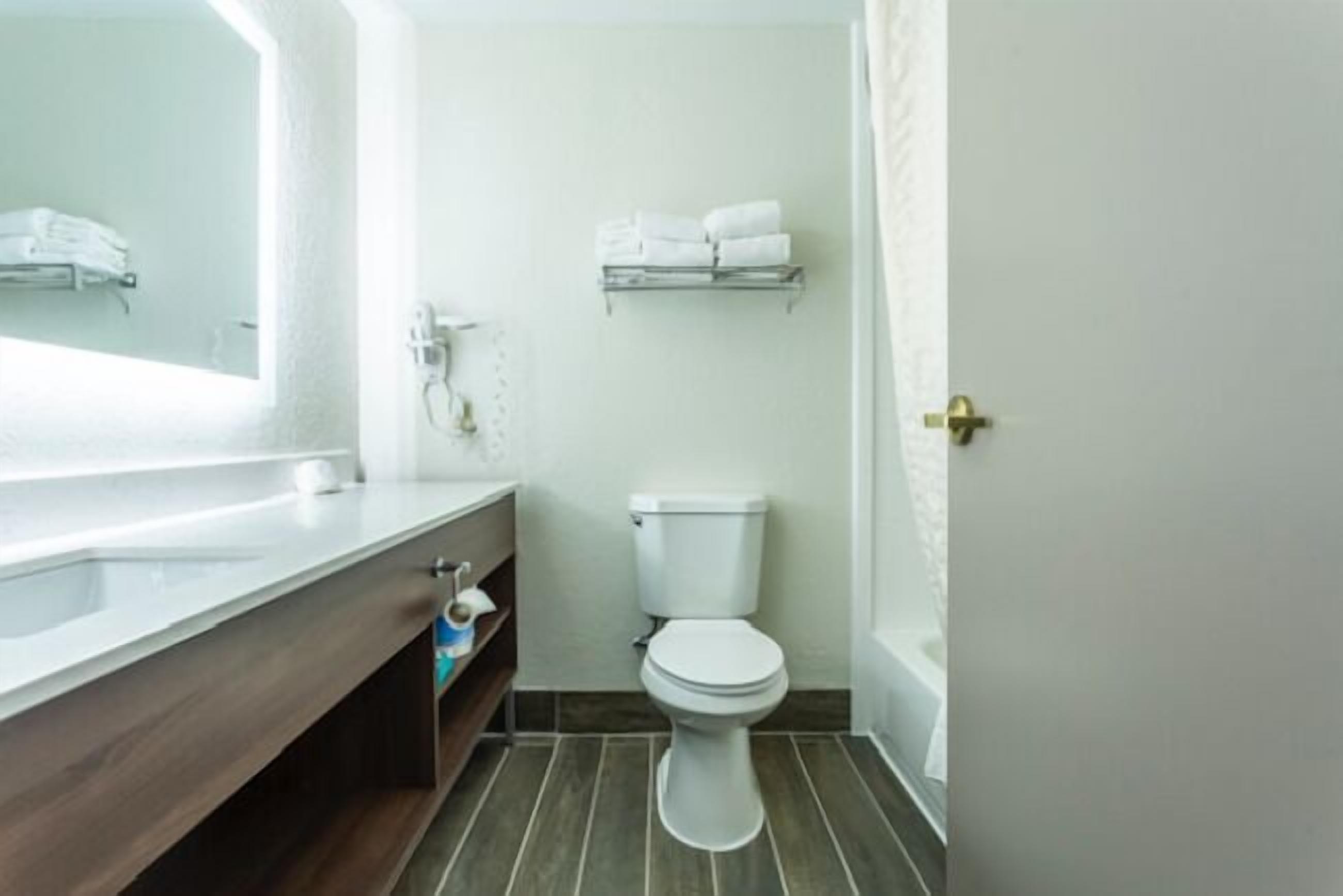 A bathroom with a white toilet, a wooden vanity, a mirror, and a towel rack.