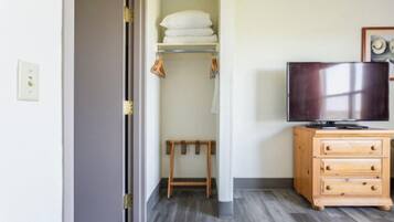 Una habitación con un aparador de madera, un televisor, un estante con toallas dobladas y un taburete de madera.