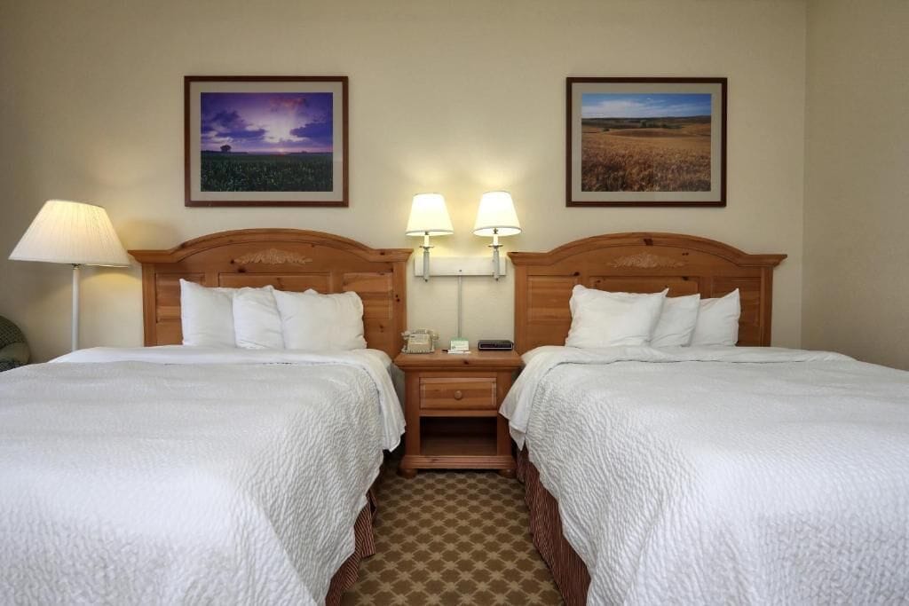 A hotel room with two single beds, a nightstand with a lamp, and two framed pictures on the wall.