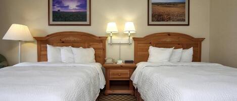 A hotel room with two single beds, a nightstand with a lamp, and two framed pictures on the wall.