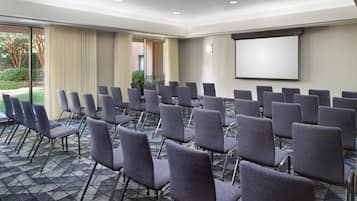 A conference room with rows of chairs, a projector screen, and a large window with curtains.