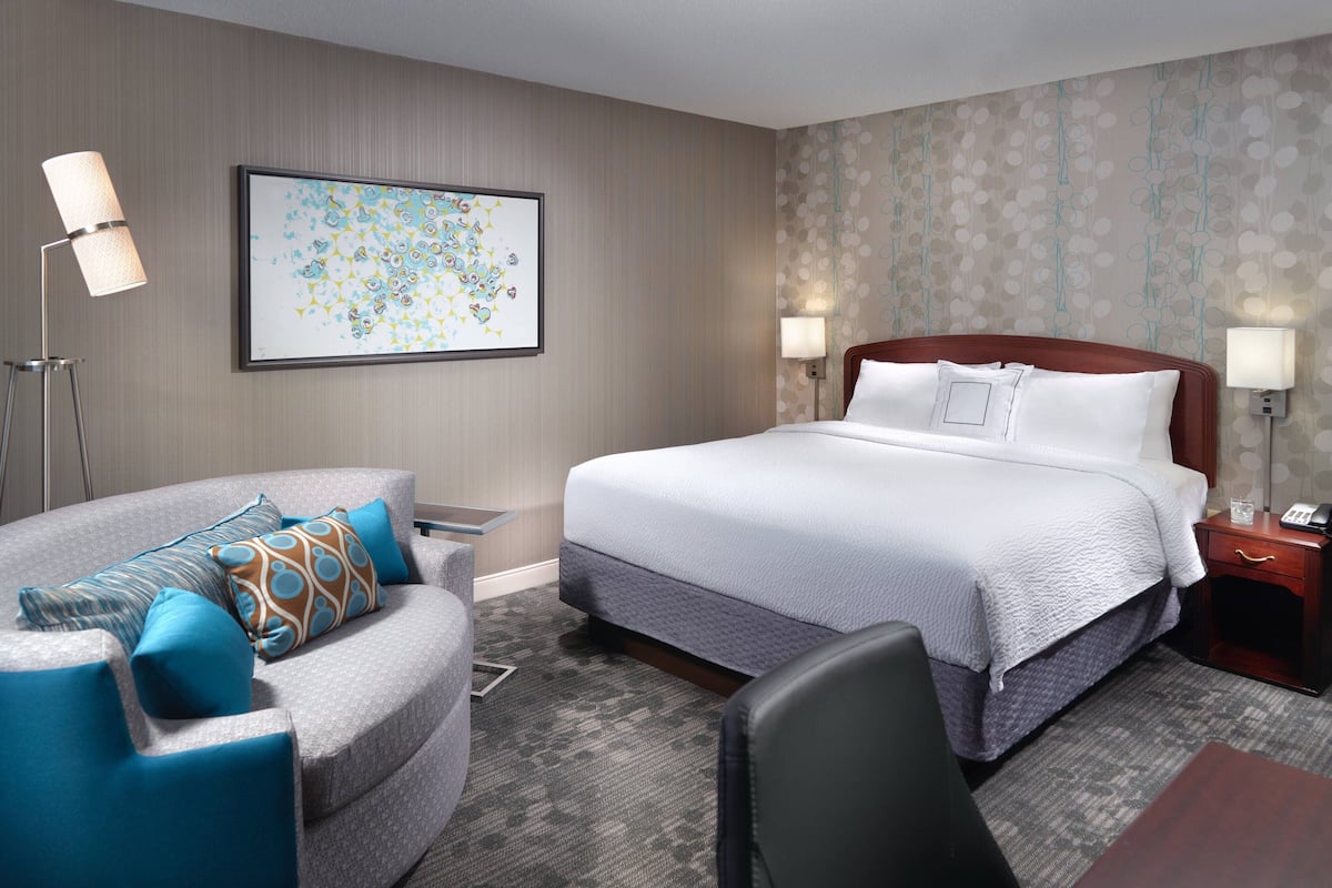 A hotel room with a bed, a chair, a desk, and a lamp.