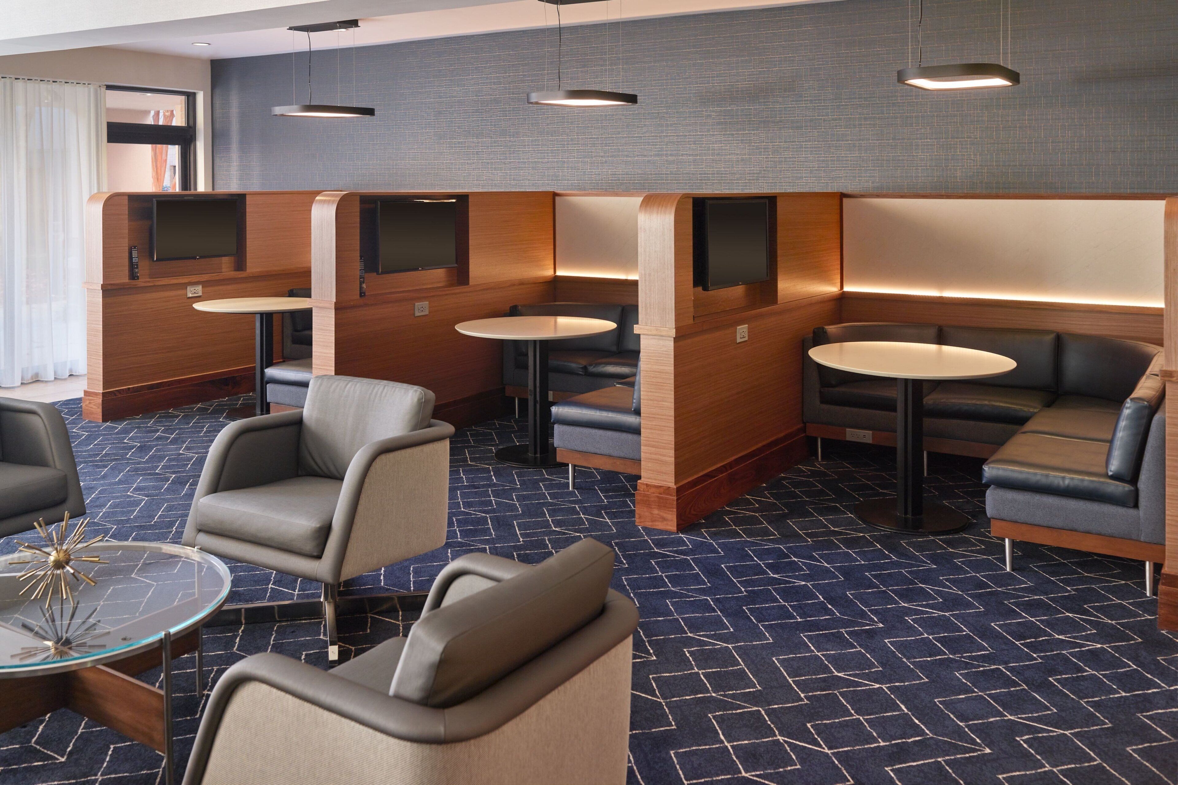 A modern hotel lobby with seating areas, tables, and a patterned carpet.