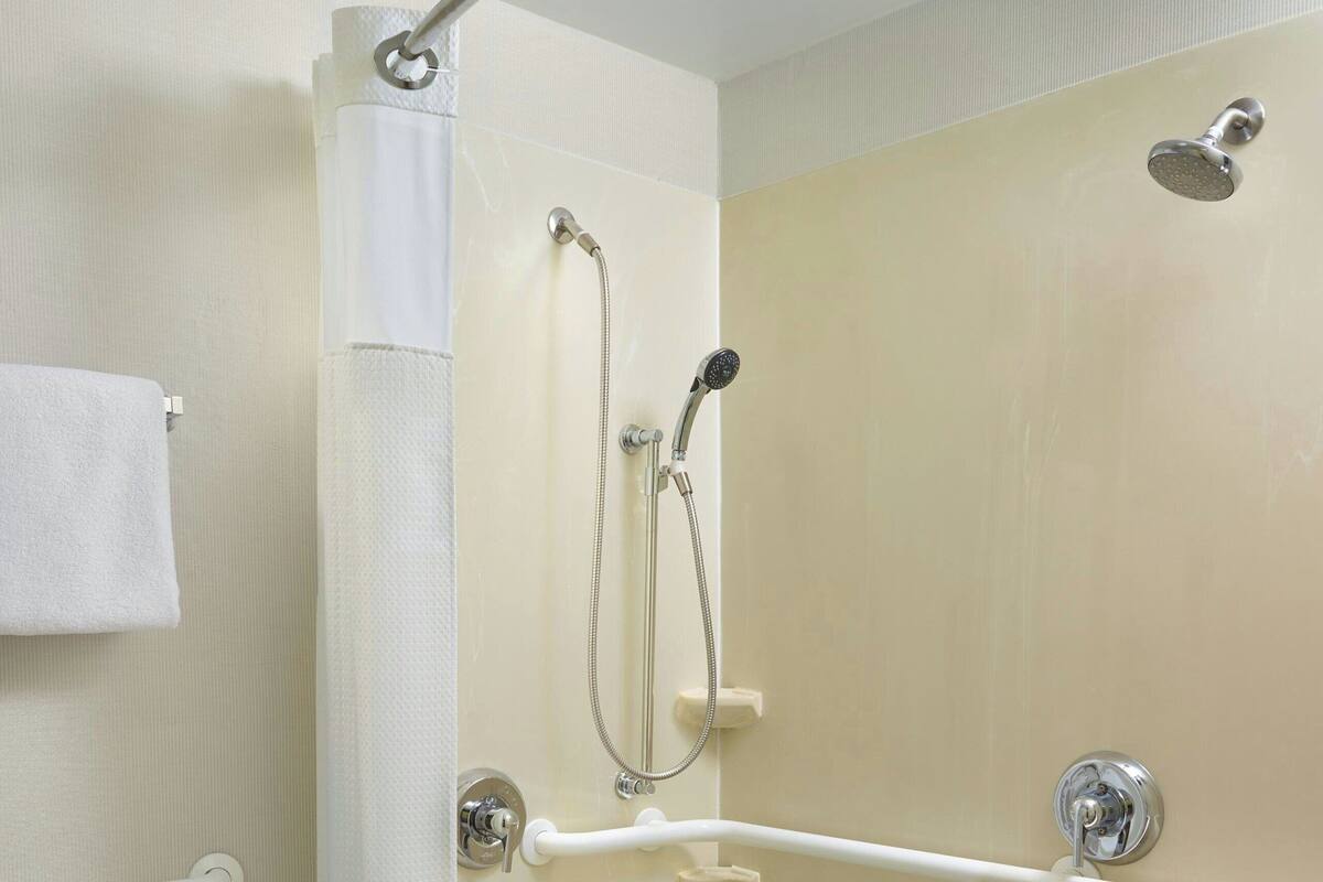 A shower area with a grab bar, a handheld showerhead, and a floor drain.