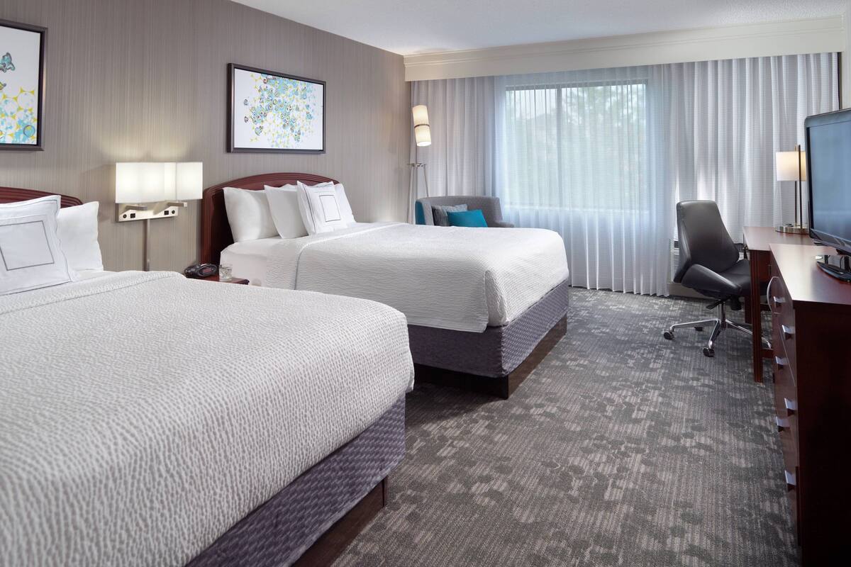 A hotel room with two beds, a desk with a TV, a chair, and artwork on the walls.