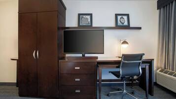 A hotel room with a dark wooden desk, a flat-screen TV, a black office chair, a desk lamp, and a wardrobe.