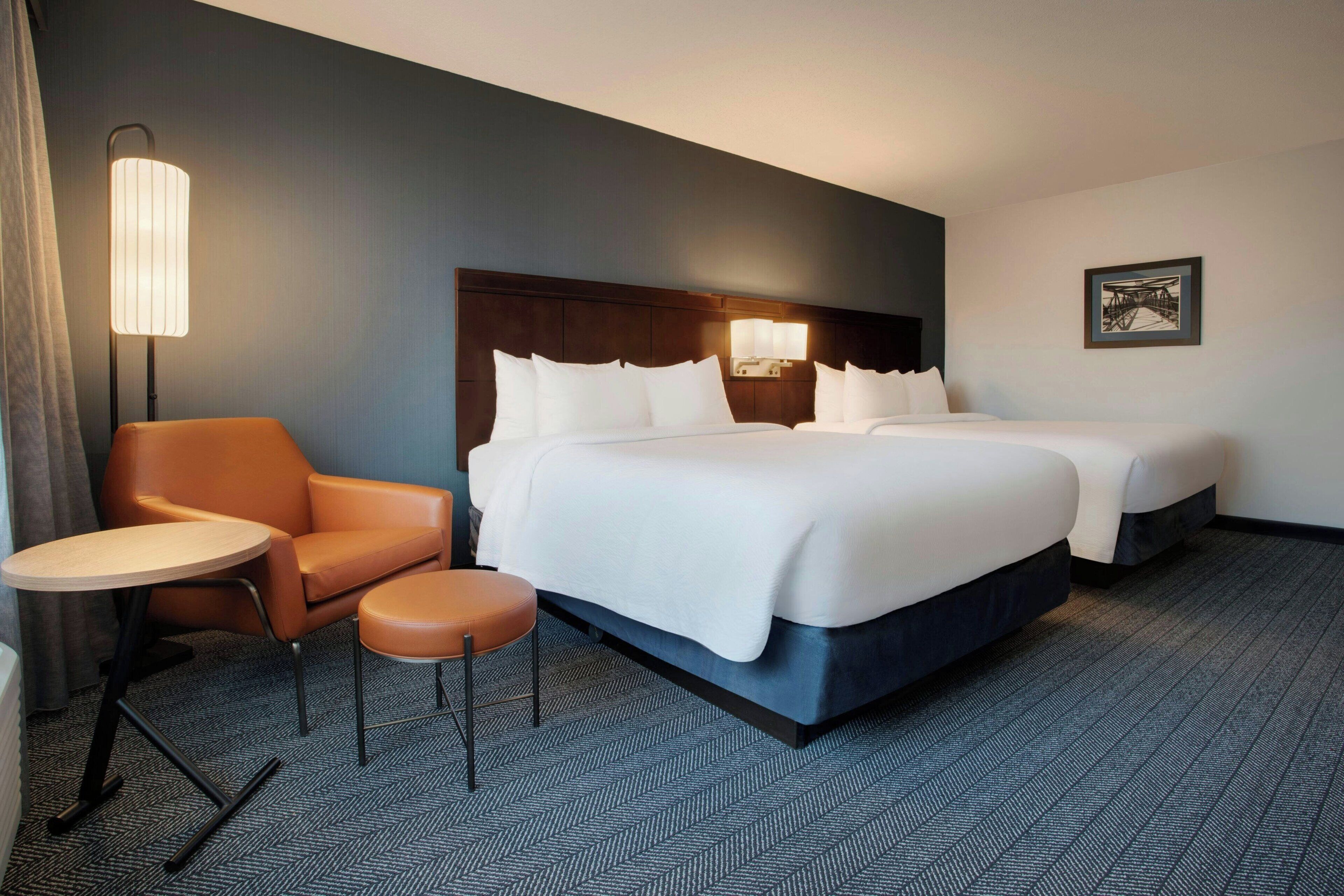 A hotel room with a large bed, two bedside tables, a chair, and a small stool.