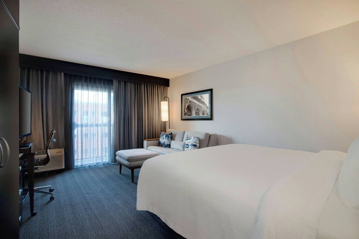Een hotelkamer met een groot bed, een bureau met stoel, een televisie en een raam met gordijnen.