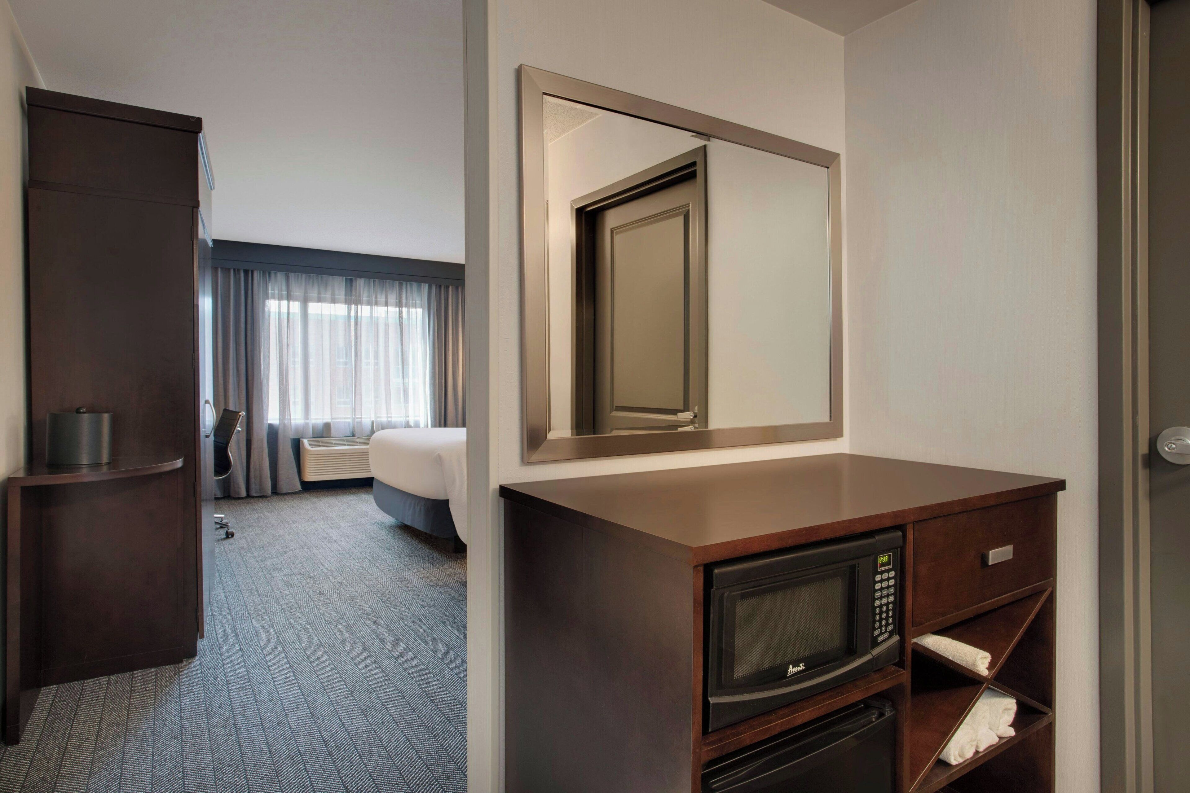Una habitación de hotel con cama, escritorio con microondas, espejo y armario.