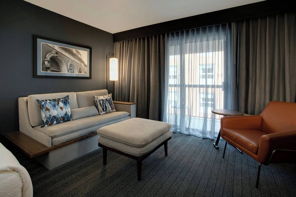 Een moderne hotelkamer met een bank, fauteuil, voetenbankje en een inlijsting foto aan de muur.