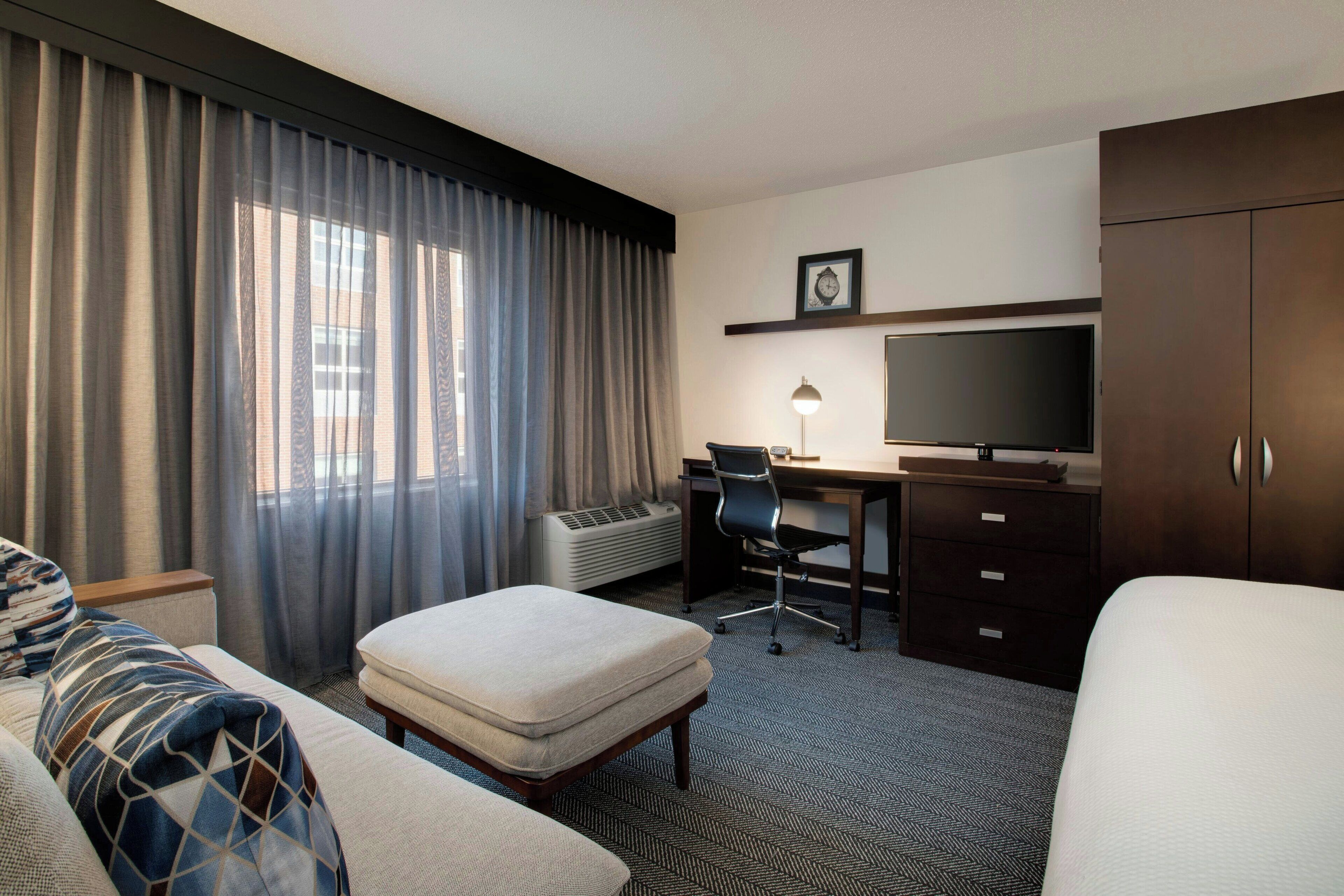 A hotel room with a bed, a desk with a chair, a television, and a wardrobe.