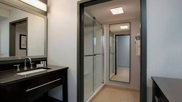 A modern bathroom with a glass shower enclosure, a dark vanity with a sink, and a large mirror.