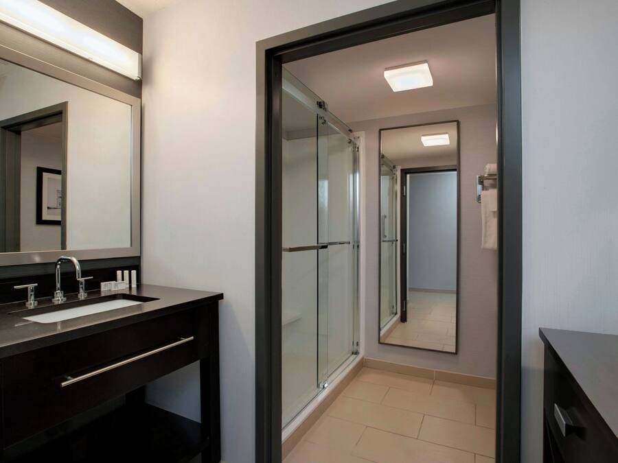 A modern bathroom with a glass shower enclosure, a dark vanity with a sink, and a large mirror.